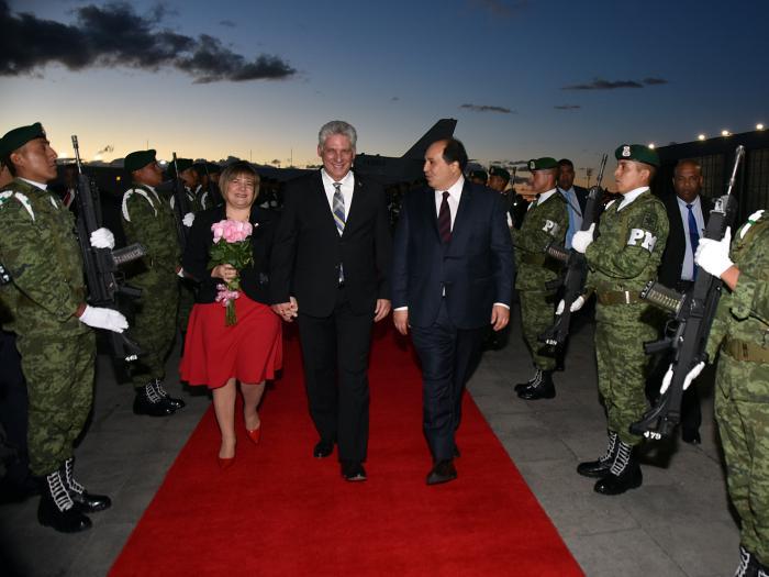 la imagen muestra a tres personas caminando sobre una alfombra roja y a varios militares custodiando
