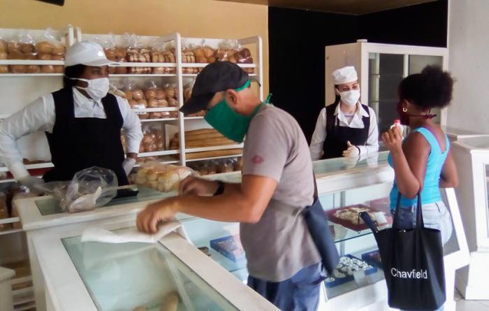 personas comprando pan y dulces en una panaderia 