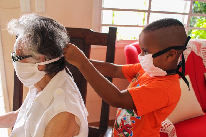 niño poniendo un nasobuco o mascarilla a su abuela