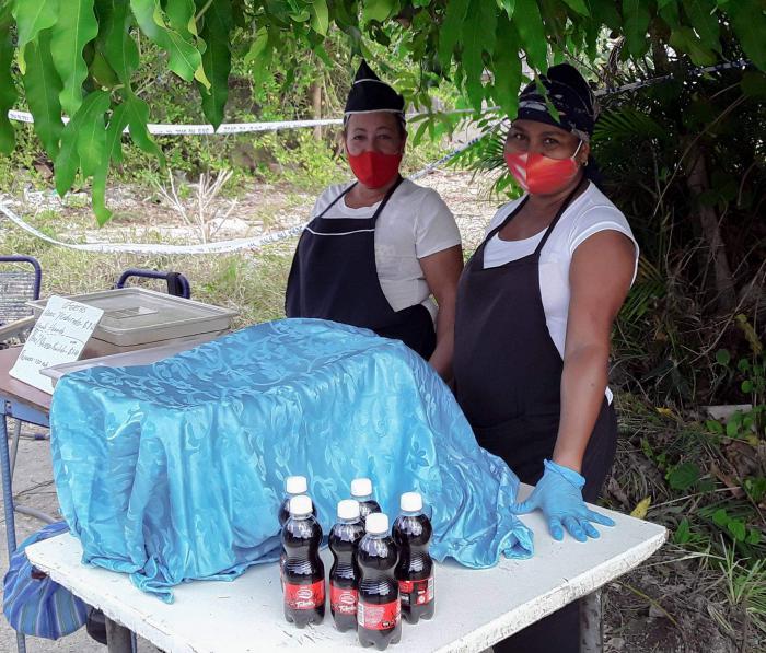 Dos dependientes que atienden la gastronía, pomos de refresco en una mesa y una caja tapada