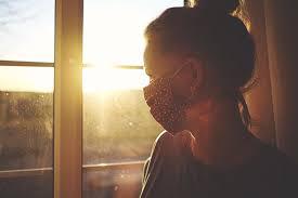 una mujer con masacarilla mira por la ventana 