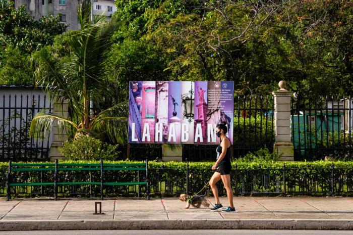 Una muchacha camina con su mascota, un perro por una calle de La Habana Vieja, se observa un cartel de La Habana