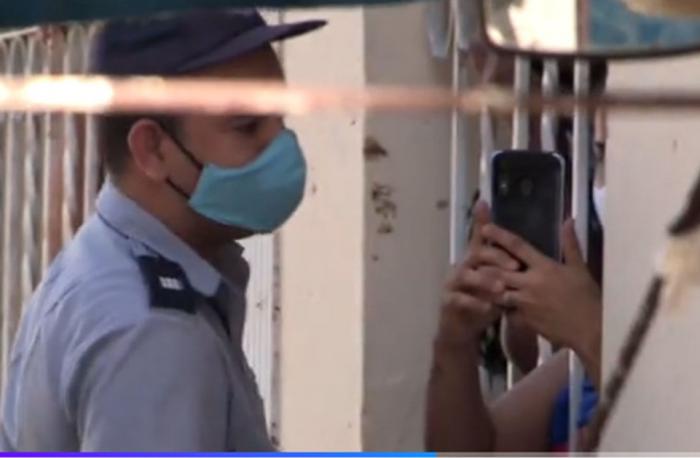 Un policía, detrás de una reja se observan unas manos con un móvil