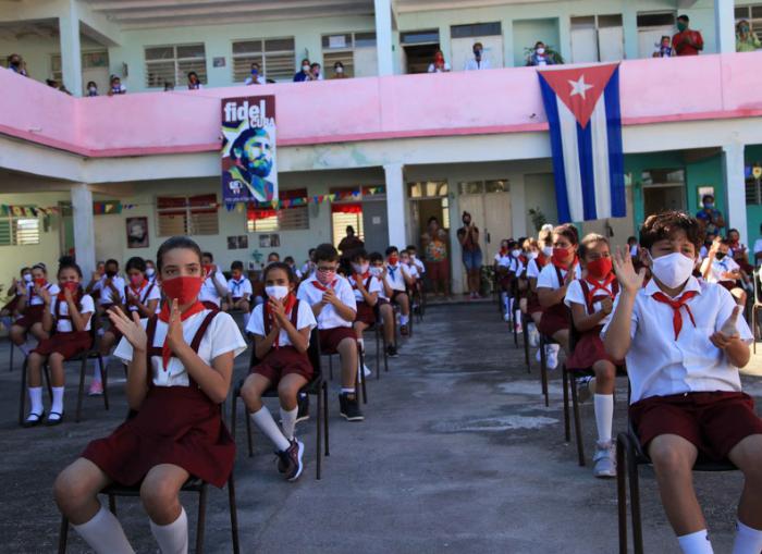 Pioneros de primaria con nasobucos, sentados en el patio de la escuela