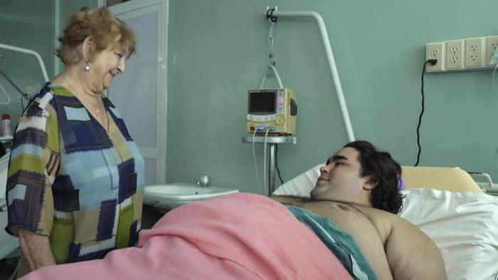 El personaje Vladimir está acostado en la cama de un hospital, al lado está parada su abuela Loló