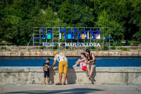 Una familia sentada en el malecón, al fondo un cartel La Habana, real y maravillosa