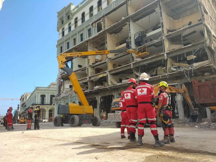 Miembros de la cruz roja frente al hotel, una grúa para sacar escombros