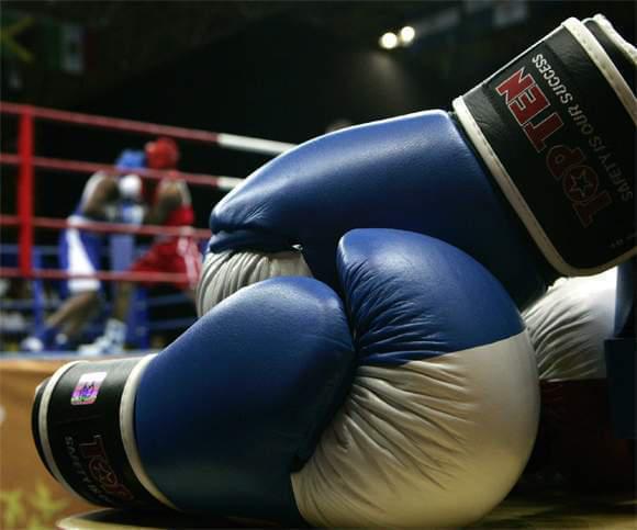 Dos boxeadores al fondo, en primer plano unos guantes de boxeo