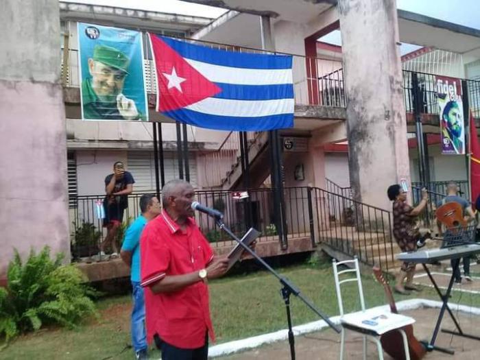 Persona hablando en el acto, al fondo un edificio con la bandera cubana
