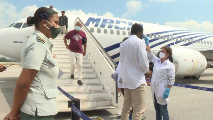 Migrantes descendiendo de un avión, personas de la aduana y personal de salud