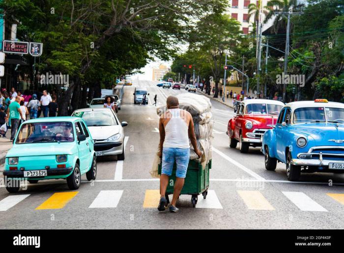 Persona en medio de la calle con una carretilla, carros alrededor