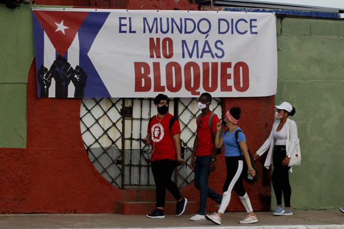Jóvenes cubanos caminan junto a un cartel alusivo al bloqueo estadounidense contra la nación caribeña  durante una actividad contra el bloqueo de Estados Unidos contra la nación cubana, convocada por la Unión de Jóvenes Comunistas de Cuba (UJC) coincidiendo con las jornadas mundiales de solidaridad con la Isla, en la occidental provincia Matanzas, Cuba. 27 de junio de 2021.Foto: Jorge Luis Baños/IPS