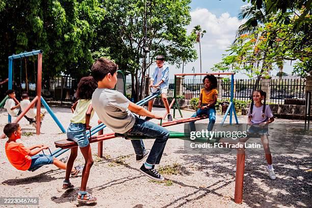 Child friends playing on seesaw at public park. Niños jugando en un parque.